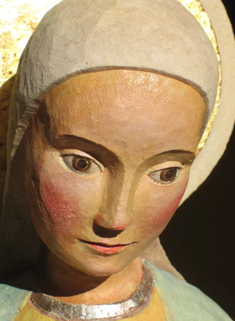Gros plan sur le visage serein d'une statue en bois polychrome de la Vierge Marie, les yeux baissés en signe de contemplation. Art sacré chrétien.